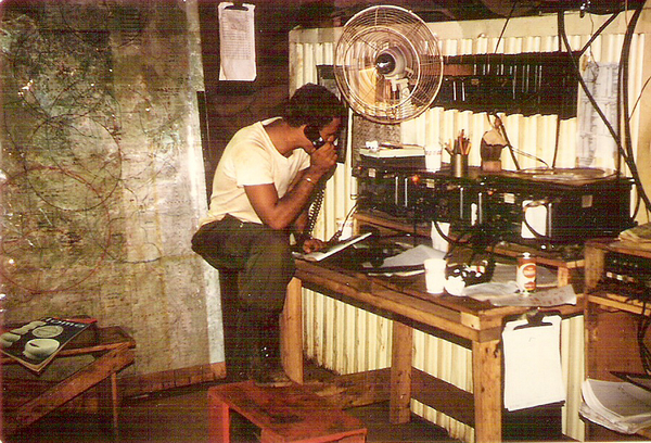 FDC TOC - LZ Oasis
Summer, 1968.  Glen Bruney on duty here.  This bunker was a complex of rooms made from CONEX containers.  These were our main radios on command freq.  Switchboard to DivArty at right.  Command map at left showing battery circles (ranges).  Plastic overlays used to plot targets & troop locations.  Clipboard itemized arty fire missions.

