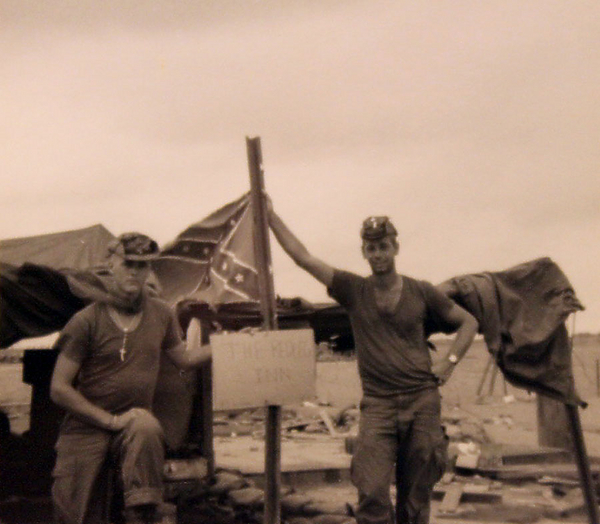 Ye Olde Redleg Inn
Sgt Lee Okerstrom, left, with Lt Monty Lafitte with a "Stars & Bars" flag in the background.  The sign reads "The Redleg Inn".  LZ English.
